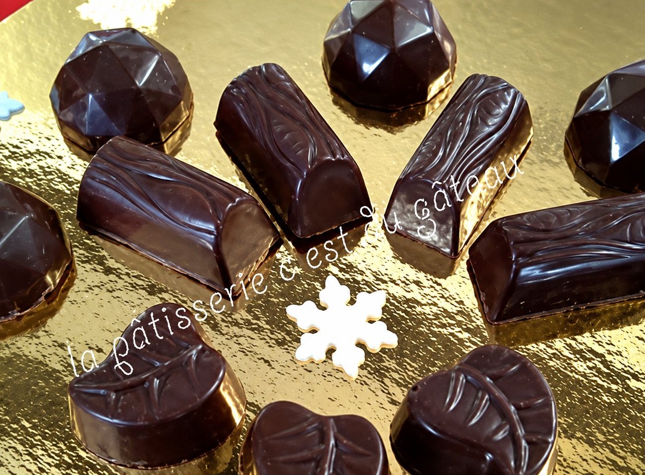 Chocolats noirs de formes variées sur un papier doré, avec un flocon blanc.