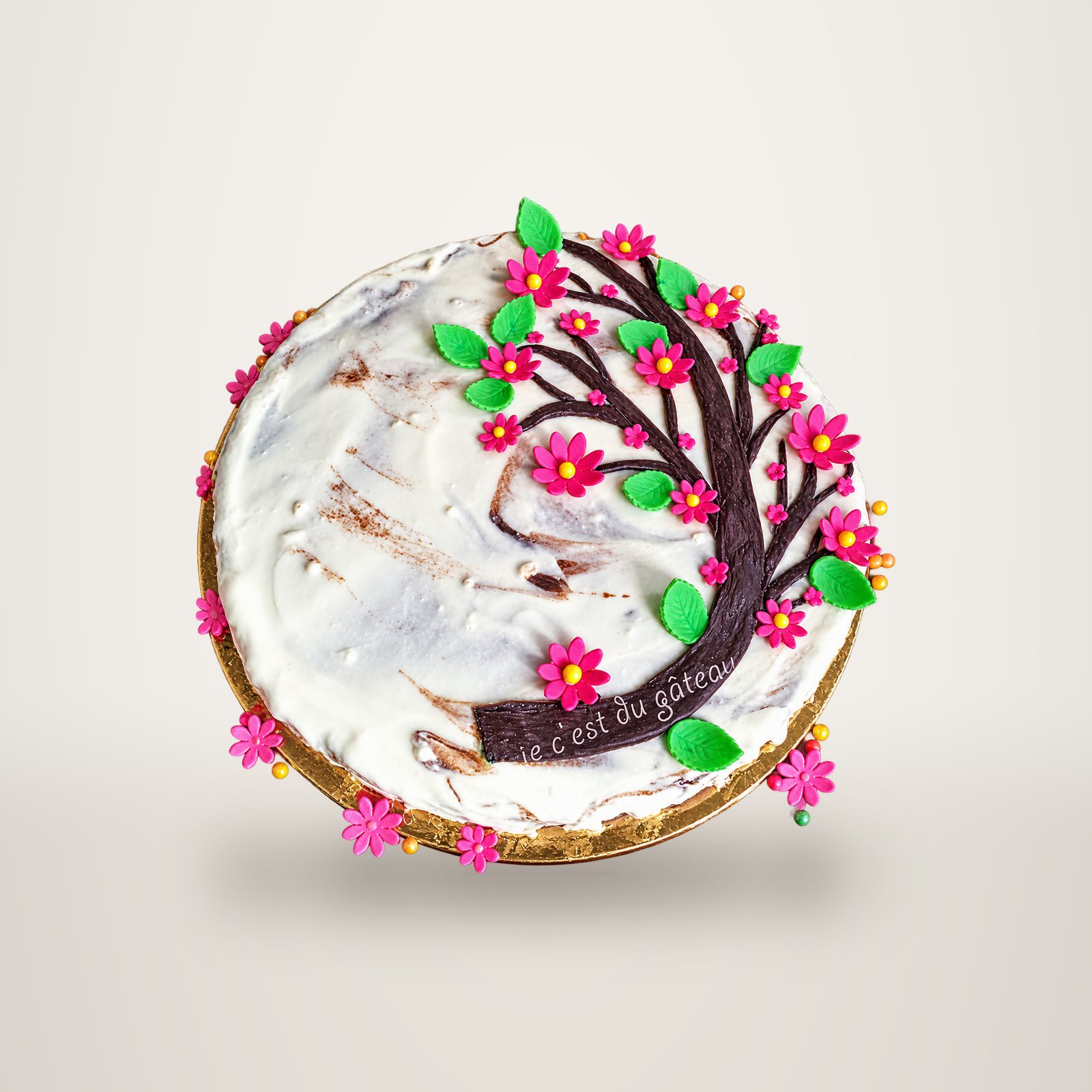 Gâteau décoré d'un arbre à fleurs roses et feuilles vertes en pâte à sucre.