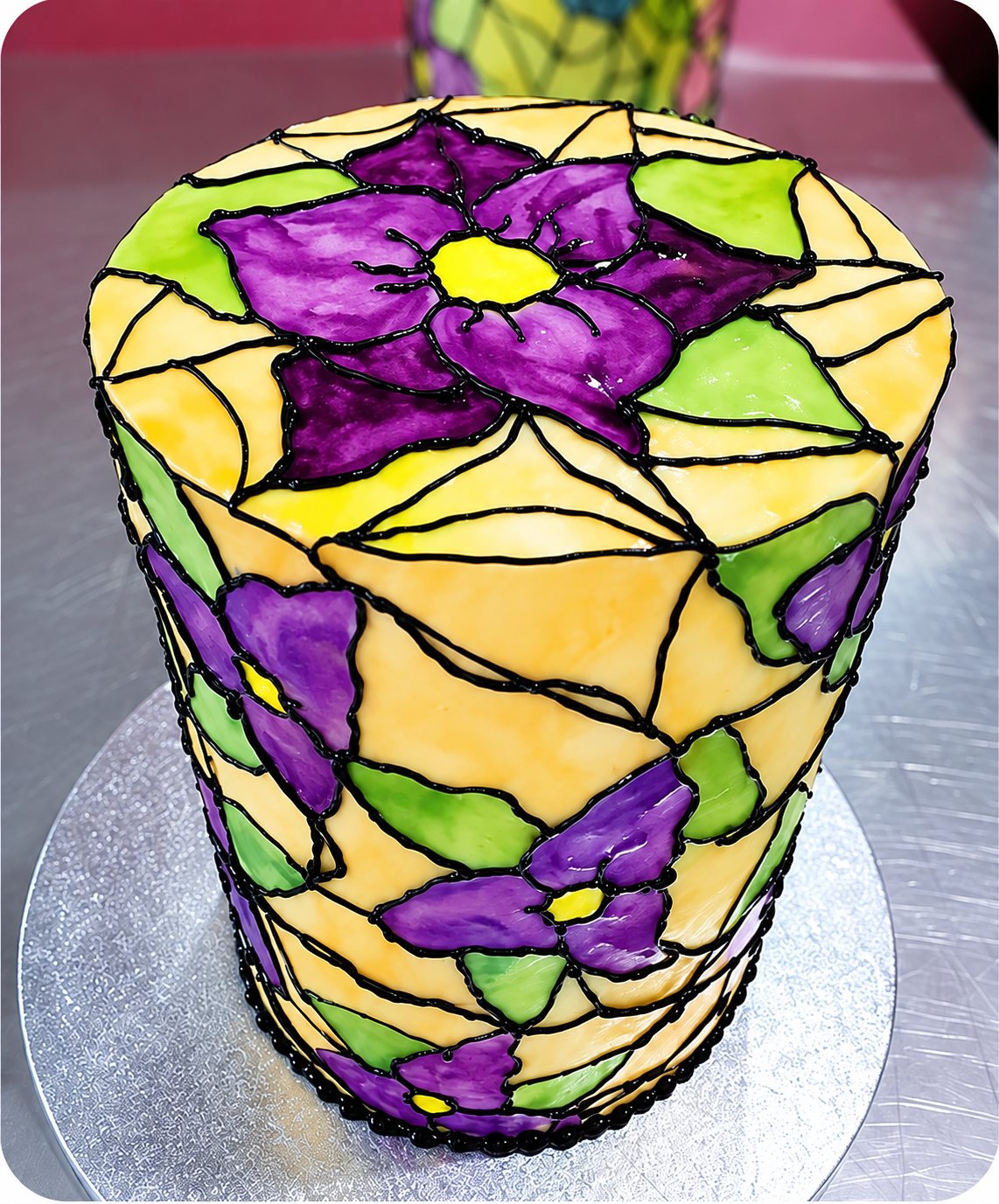 Gâteau peint à la main, effet vitrail, avec de grandes fleurs violettes, posé sur un plan en acier.