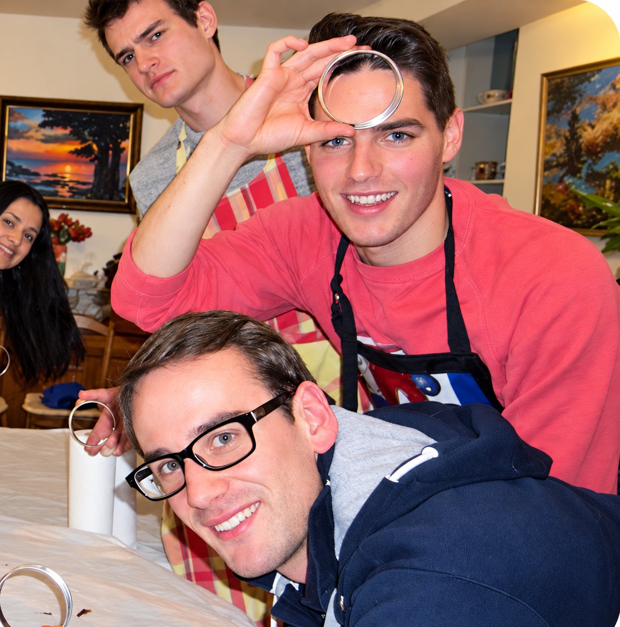 Trois jeunes hommes rieurs, des anneaux de pâte devant les yeux, autour d'une table d'atelier.