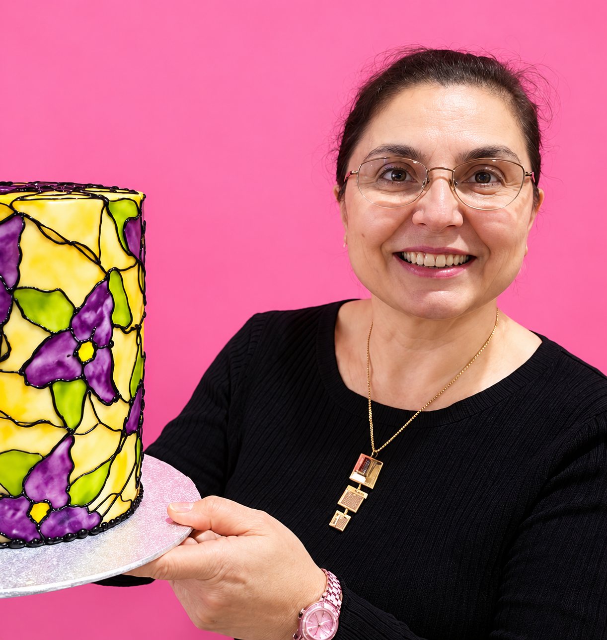 Kristina Silianova, pâtissière, souriante, tient un gâteau peint à la main à l'effet vitrail.