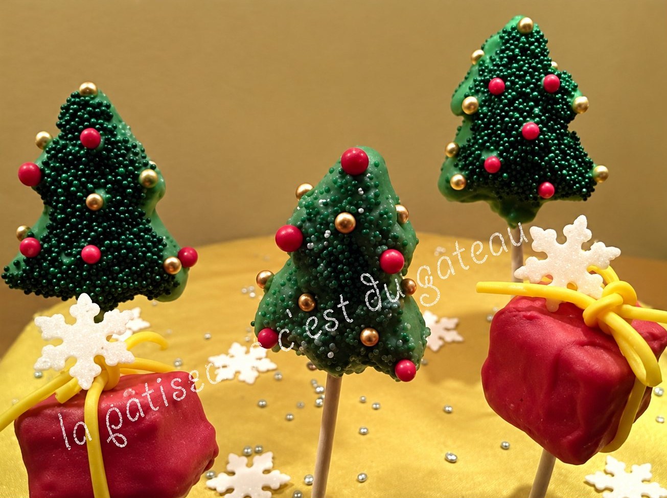 Cake pops de Noël en forme de sapins et de paquets cadeaux, avec des flocons blancs.
